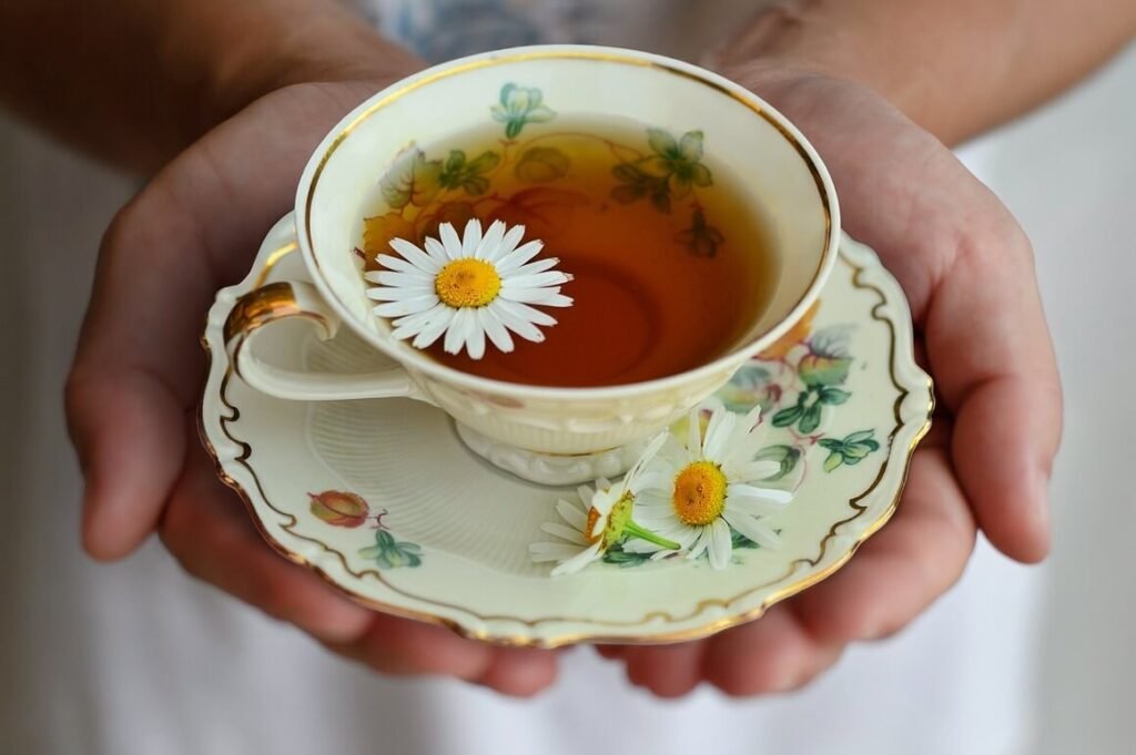 a person presenting a chamomile tea cup with a german chamomile flower on the cup