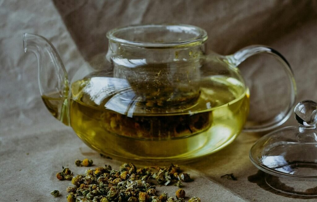 a glass teapot with chamomile infused and loose leaves scatred around