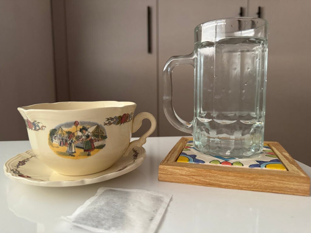 A cup of water next to a cup of tea with a tea bag