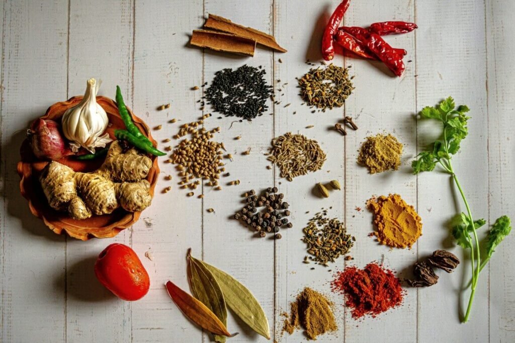 A variety of spices and herbs are artfully arranged on a white wooden surface